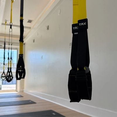 Yellow TRX suspension trainers hanging in a gym with mats on the floor.