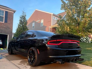 Sleek black Dodge Charger parked on a driveway during sunset.