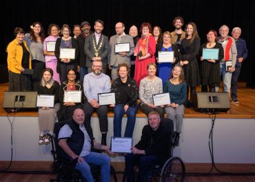 Group photo of award recipients holding certificates on stage.