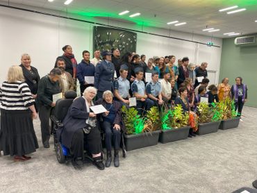 A group photo of diverse people, including uniformed officers, holding certificates at a ceremony.