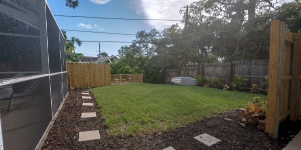 Sunny backyard with green grass and wooden fence.