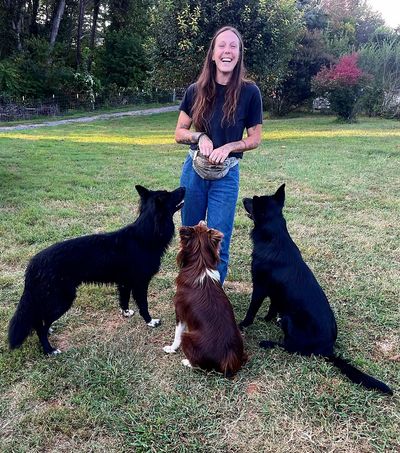A woman joyfully trains three attentive dogs outdoors on a grassy field.