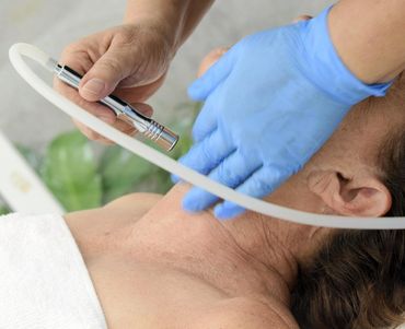 A person receiving a facial treatment with a handheld device and gloved hands.