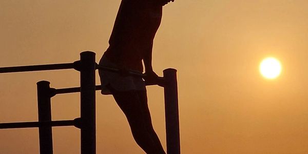 Silhouette of a person exercising on parallel bars at sunset.
