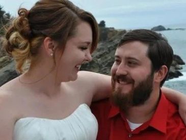 A couple smiling at each other by the coast.