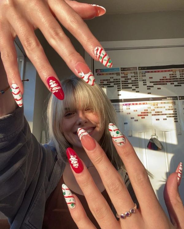 Smiling woman shows off festive red, white, and green Christmas-themed nails.