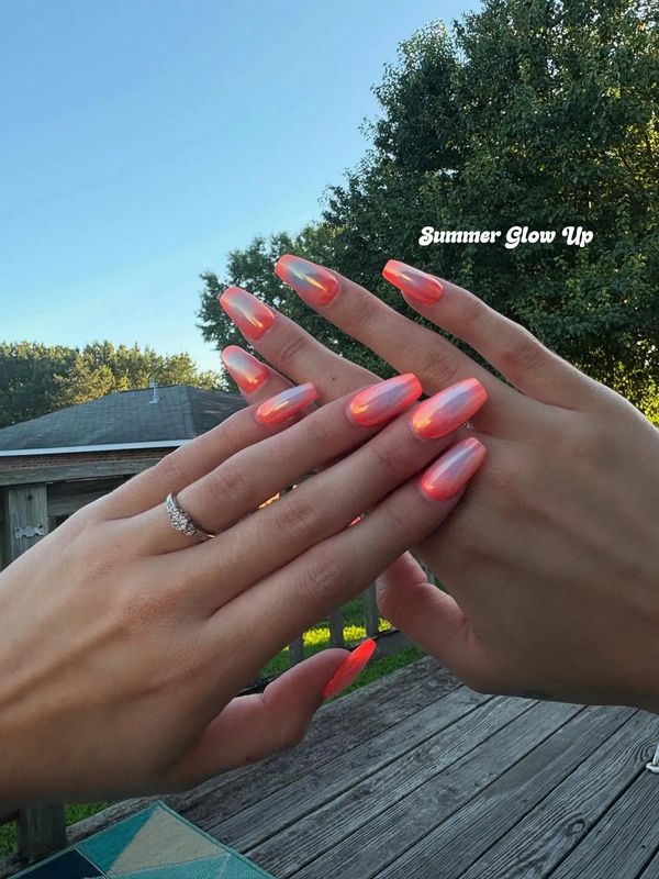 Hands with long, glowing orange-pink nails under natural sunlight outdoors.