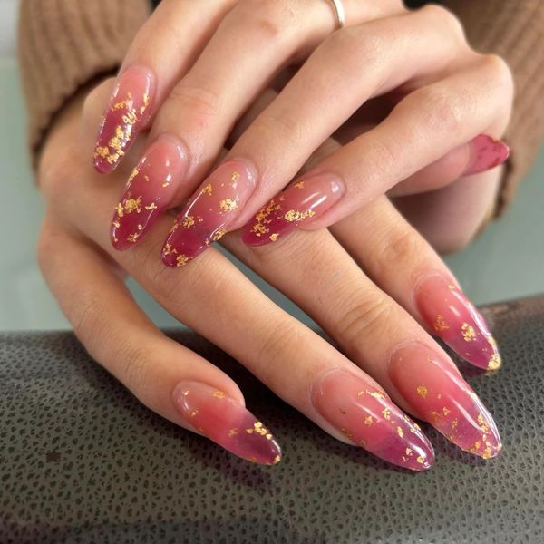 Long almond-shaped nails with a pink ombre and gold foil accents.