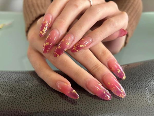 Long almond-shaped nails with a pink ombre and gold foil accents.