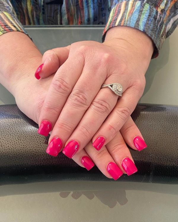 Well-manicured hands with bright pink nails and a sparkling ring.