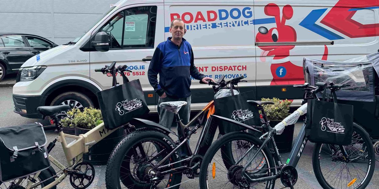 a man standing beside e electric bikes, with a delivery van behind him