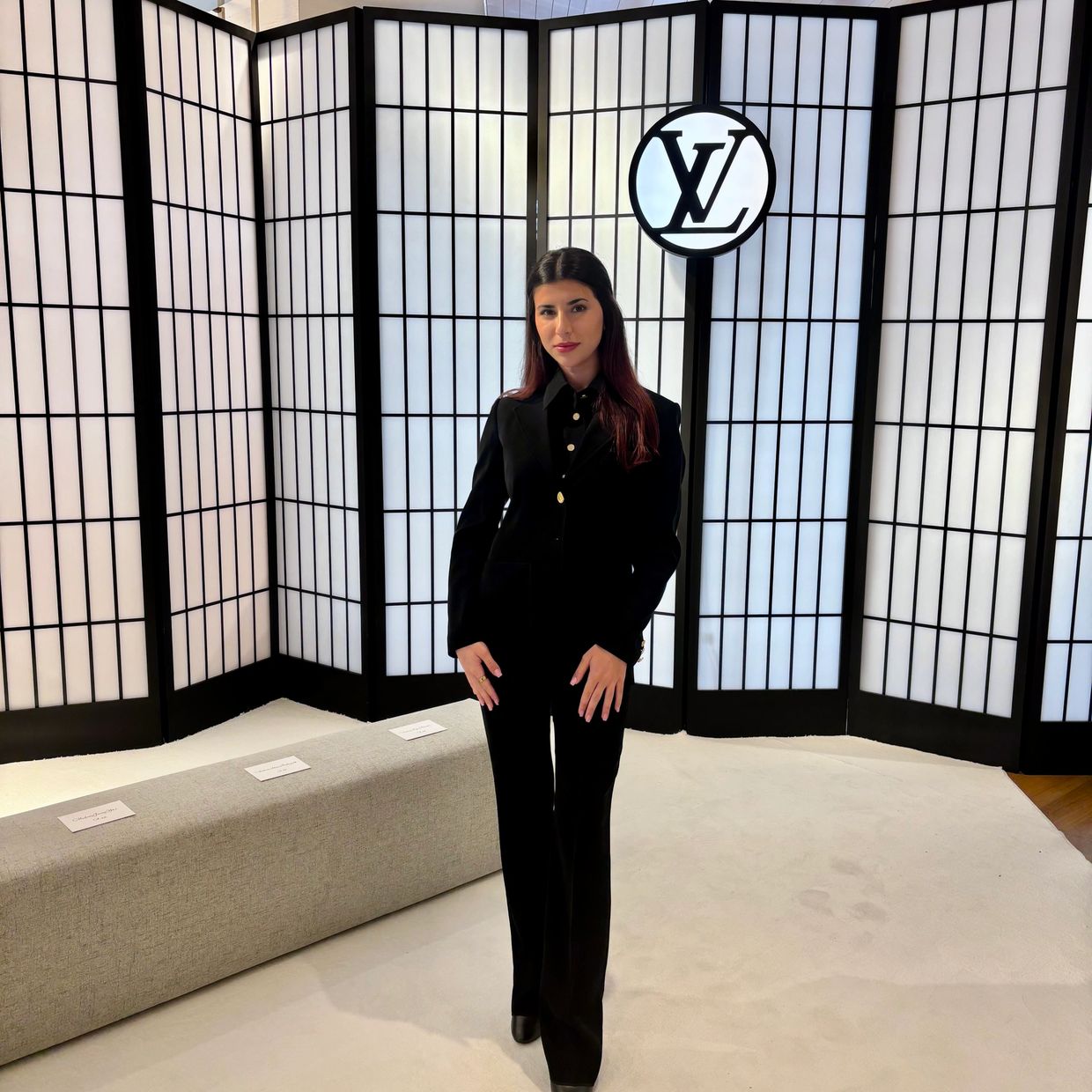 Woman in a black suit posing in front of a Louis Vuitton backdrop.