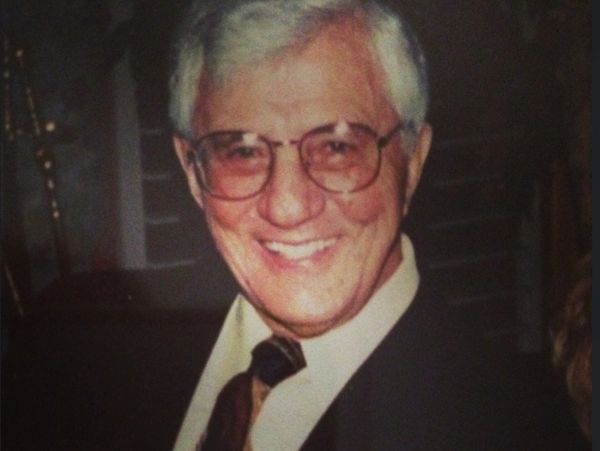 An elderly man smiling warmly, wearing glasses and a suit.