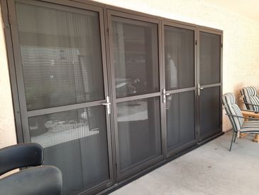 Four black metal-framed screen doors on a patio with chairs nearby.