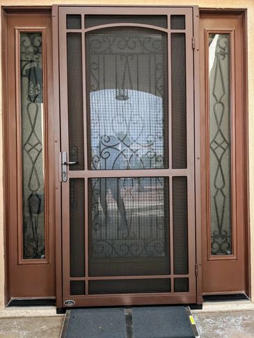 A brown metal screen door with decorative glass panels on each side.