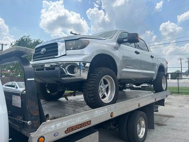 Silver Toyota Tundra pickup on a tow truck under a cloudy sky.