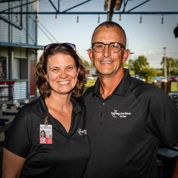 Two smiling professionals wearing matching black polo shirts in a casual indoor setting.