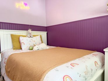 Cozy purple-themed bedroom with unicorn bedding and a 'good vibes' neon sign.