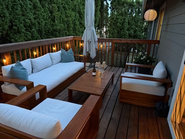 Cozy outdoor seating area with wooden furniture and soft cushions on a deck surrounded by greenery.