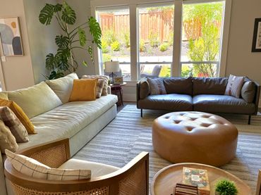 Bright living room with modern sofas, a large potted plant, and a round leather ottoman.
