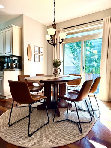 Sunlit dining area with brown chairs and a wooden table on a round rug.