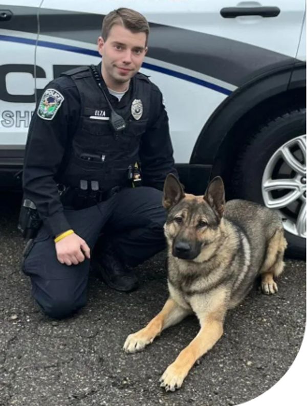 Police officer kneeling next to a German Shepherd K9 unit by a patrol car.