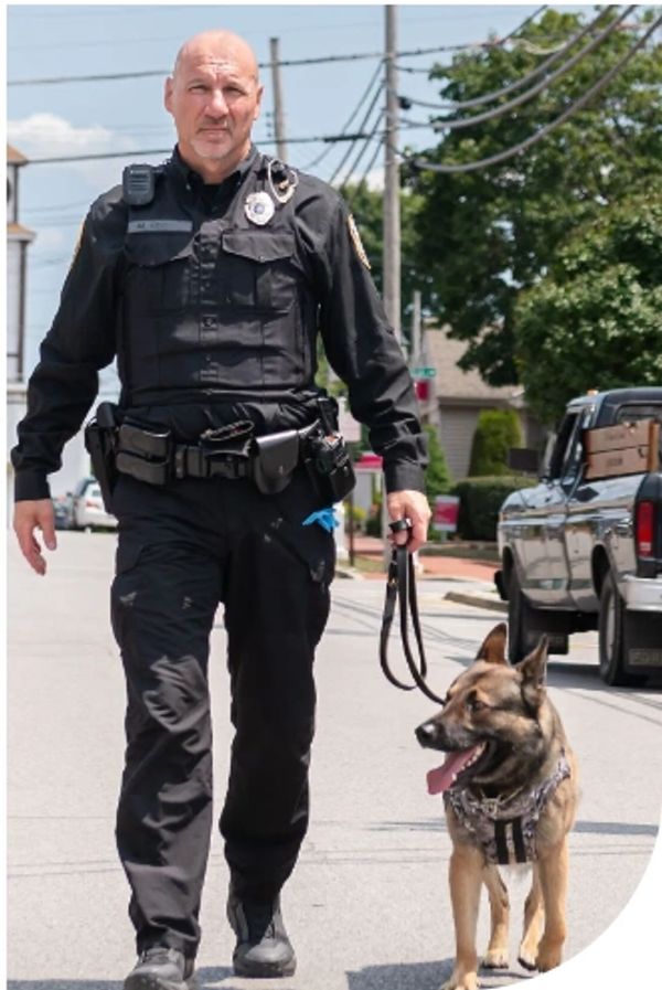Police officer walking a German Shepherd K9 dog on a street.