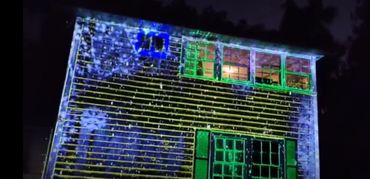 Colorful light projections illuminate a house exterior at night.