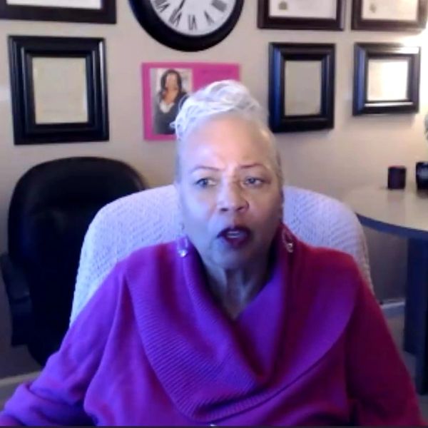 Older woman in a magenta sweater speaking indoors.