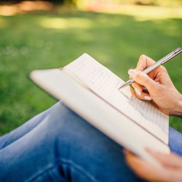 Person writing in a mental health workbook outdoors.