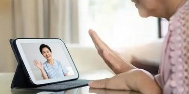Two women video chatting on a tablet, waving at each other.