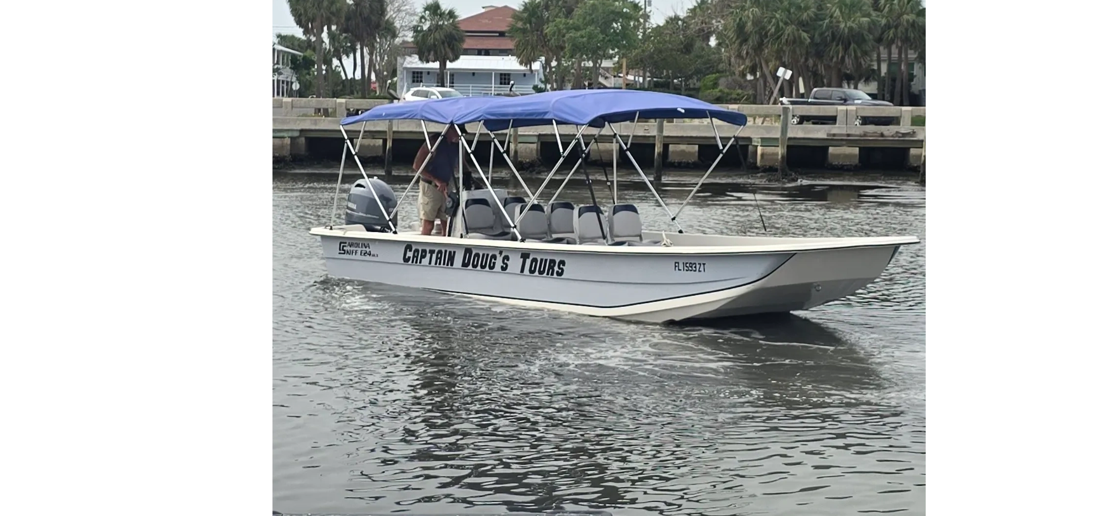 A boat named Captain Doug's Tours with blue canopy on a waterway near a dock.