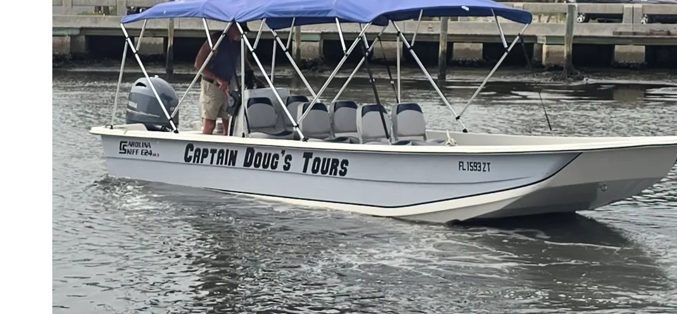 A boat named Captain Doug's Tours with blue canopy on a waterway near a dock.