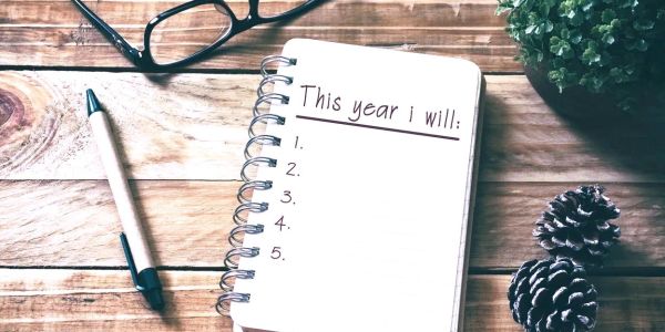 Notebook with a list template titled "This year I will" on a wooden table.