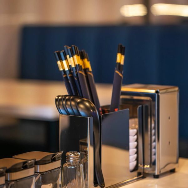 Black chopsticks and spoons in a holder on a table.