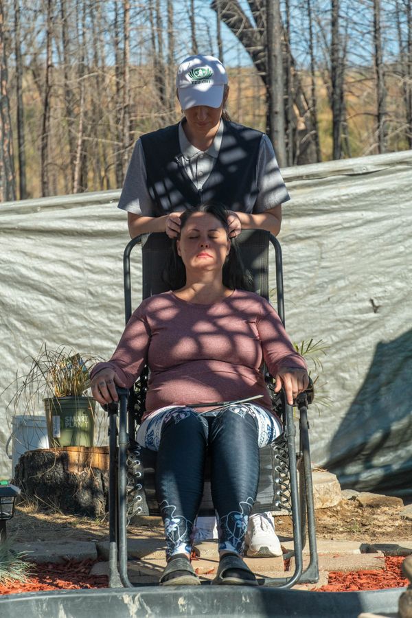 Bobbie Rae Jones massages the head of a middle-aged woman as she sits outside relaxed in a chair