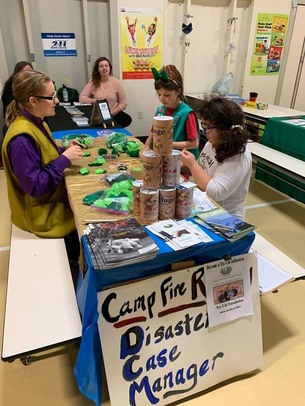 Three women and two young girls sit around a table dedicated to Camp Fire aid efforts