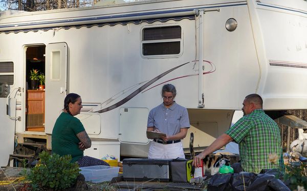 Bobbie Rae Jones stands outside of a mobile home and  speaking with two tenants
