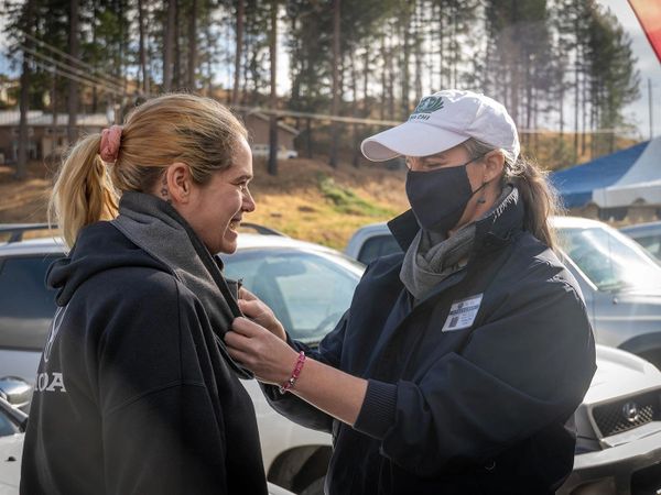 Two women smiling at one another standing in front of a row of cars