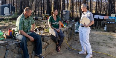 Bobbie stands as she speaks to a man and a woman seated on a short stone wall