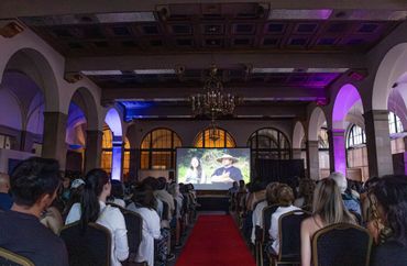 Audience watching a film in a grand hall with colorful lighting.