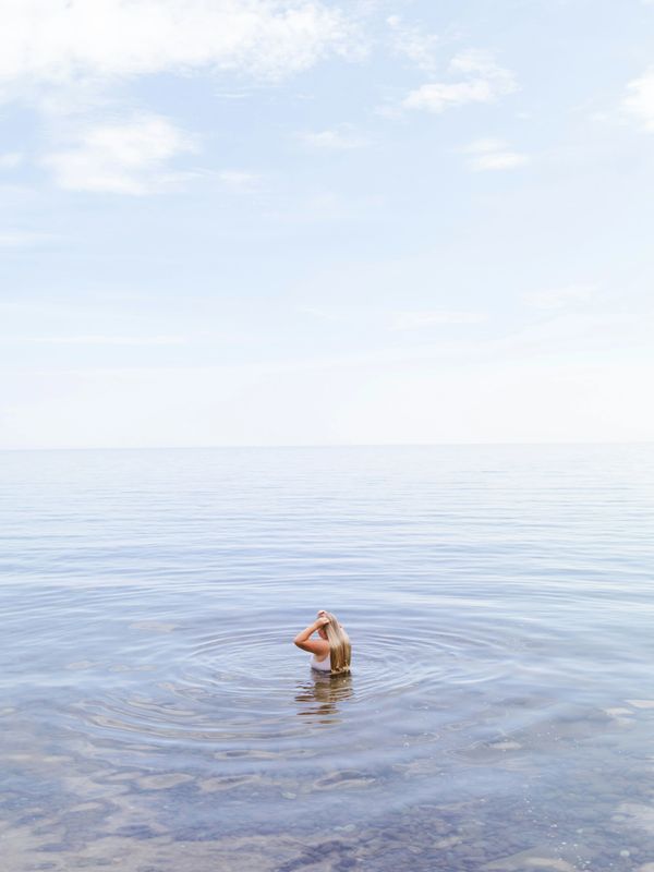 A person standing alone in calm, clear water under a bright sky.