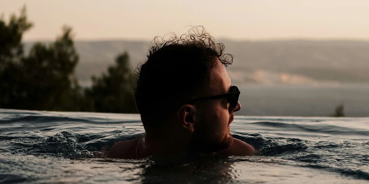 Man with sunglasses relaxing in a pool during sunset.
