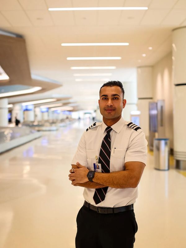 A confident pilot stands in an airport terminal with arms crossed.