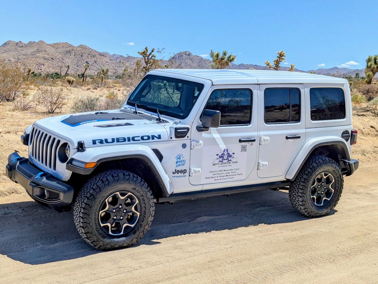 White Jeep Rubicon parked on a desert trail under clear blue sky.