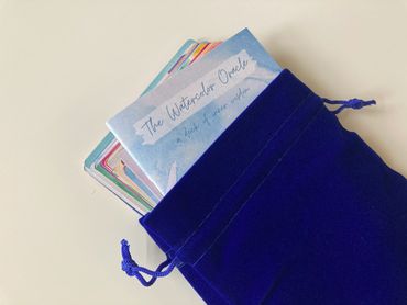 The Watercolor Oracle deck partially inside a royal blue velvet drawstring pouch.