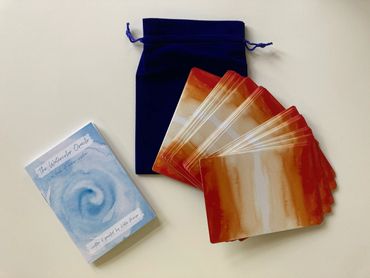 Watercolor Oracle cards with a blue velvet pouch and guidebook on a white surface.