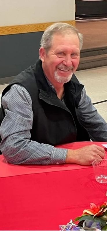 Smiling older man sitting at a table with a red tablecloth indoors.