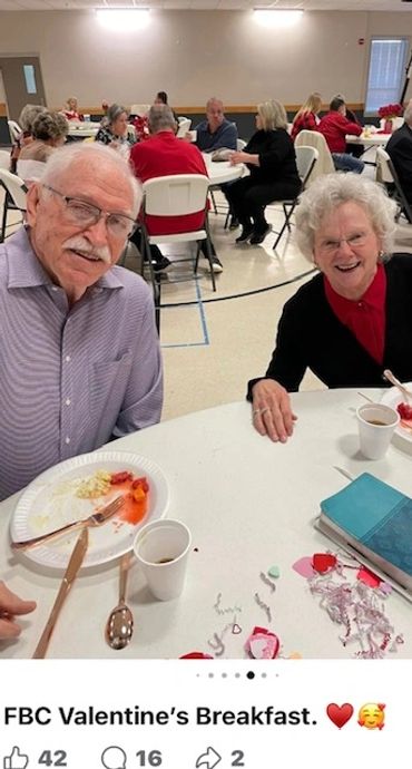 Elderly couple enjoying FBC Valentine’s Breakfast in a community hall.