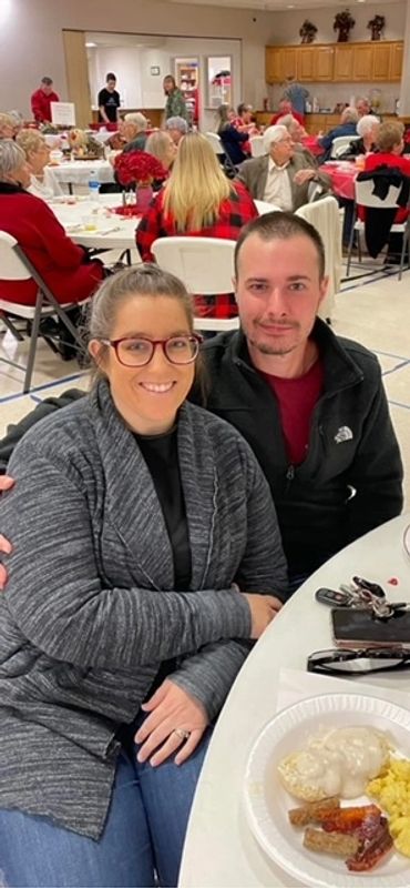 A couple smiling at a community meal event with food on their table.